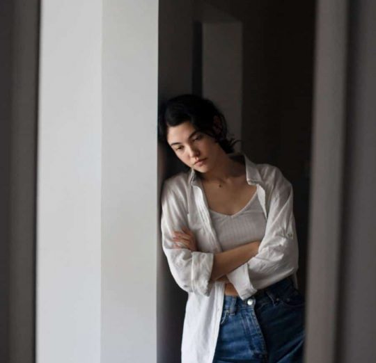 Young woman dealing with anxiety, leaning against a wall, seeking PTSD treatment and mental health support.